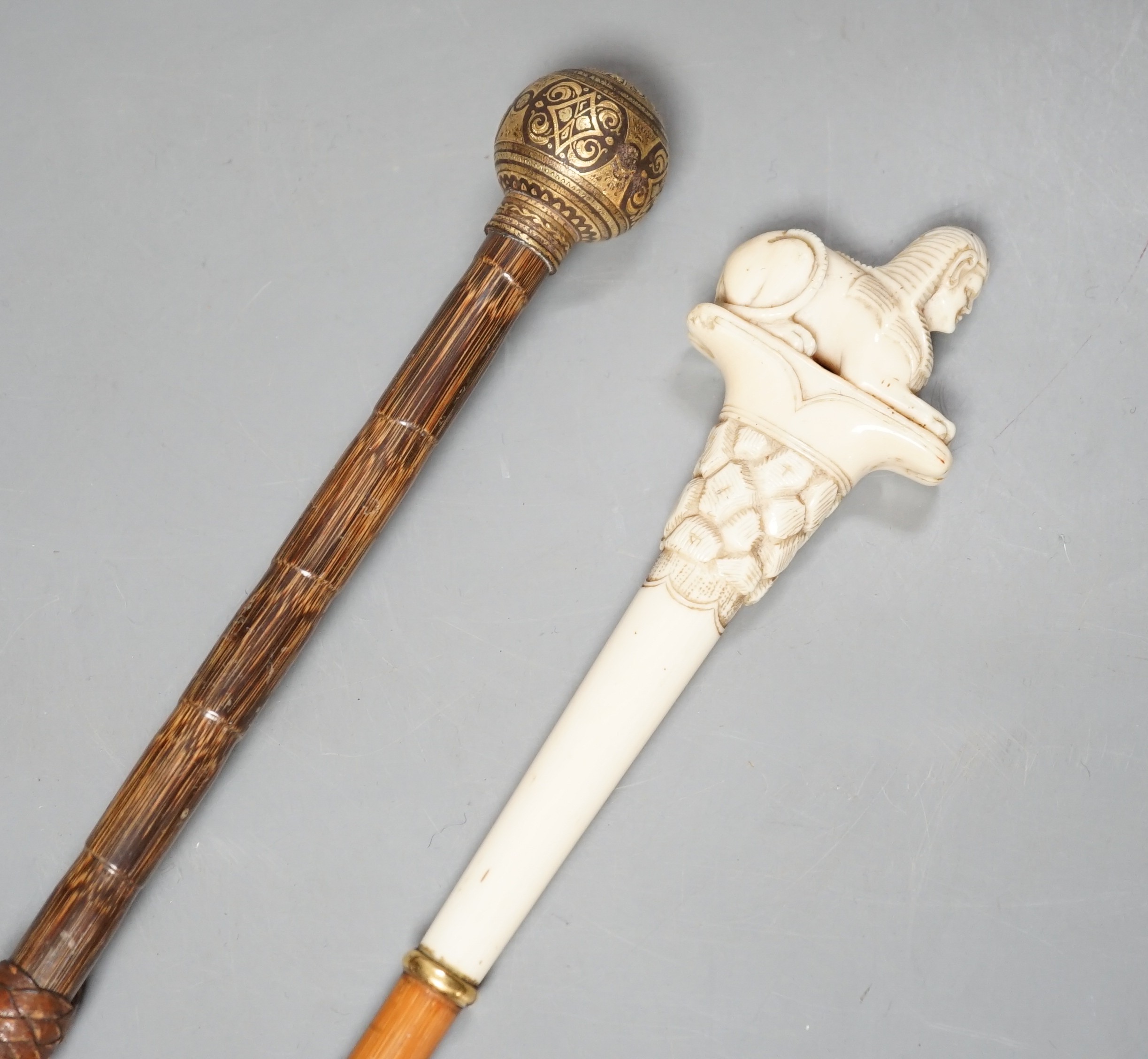 An early 20th century ivory ‘sphinx’ parasol handle, 84cm, together with another gold and iron damascened parasol handle, 62cm